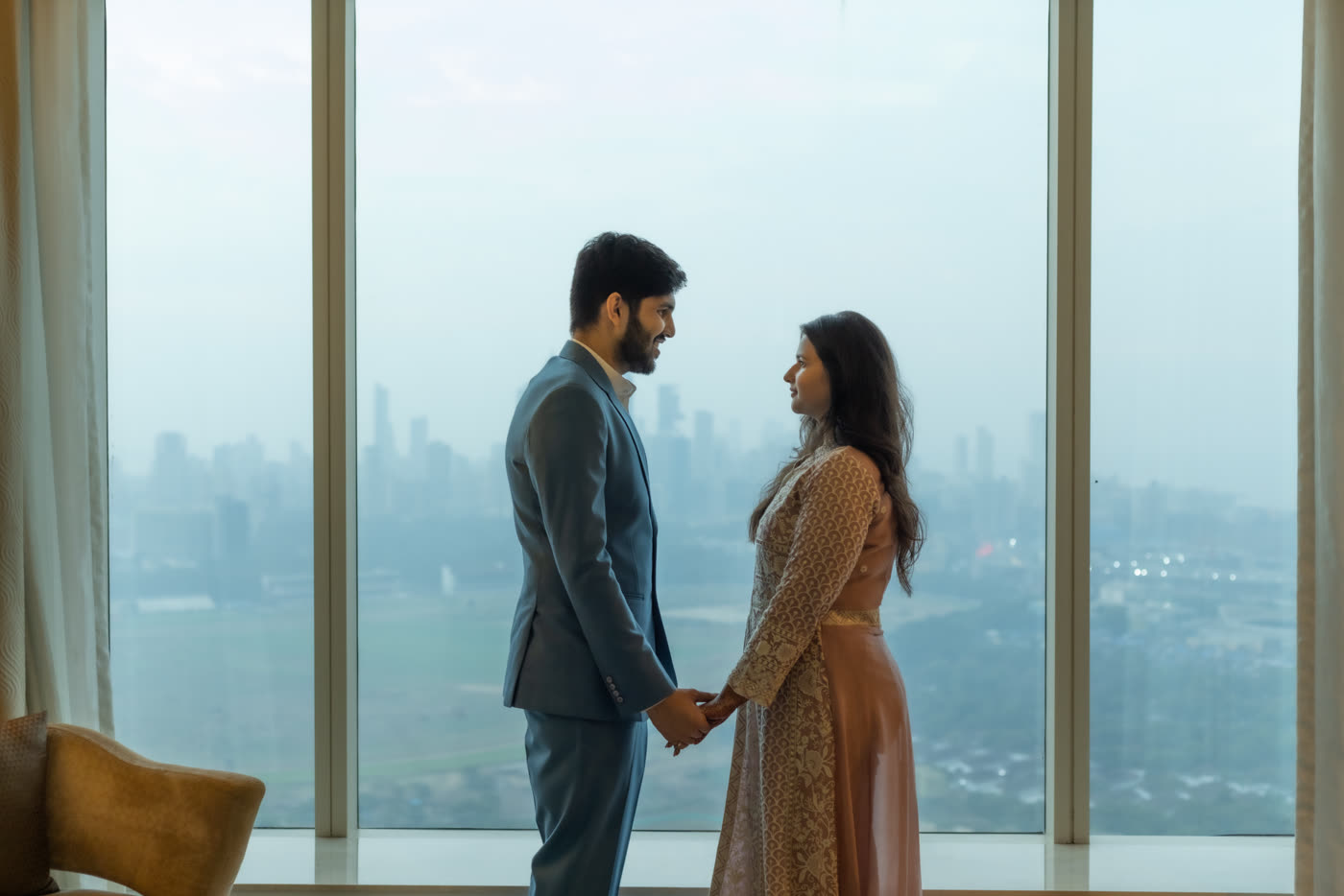 A couple holding hands by a window above the city