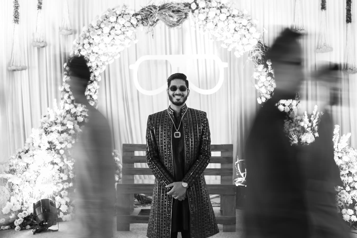 A groom beneath the floral arch, in black and white